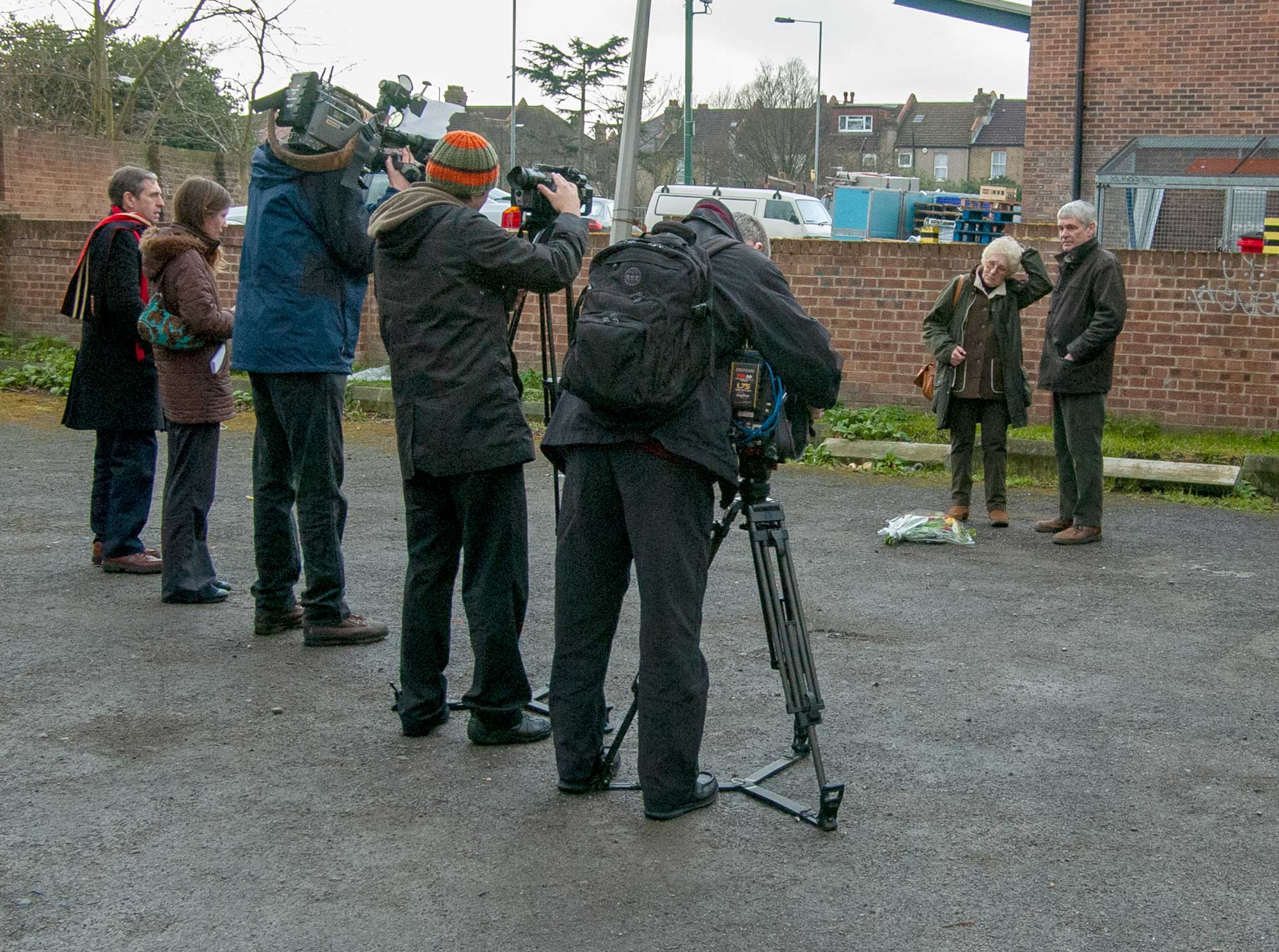TV crews and newspaper journalists respectfully look on as Isobel and Alastair lay flowers at the scene of the crime
